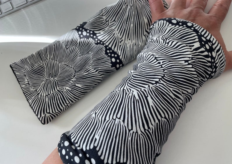 May include: A pair of black and white arm warmers with a swirling, organic pattern. The fabric has a textured, almost woven look.