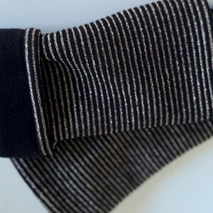 Puede incluir: Un par de calentadores de brazo a rayas negras y plateadas. Los calentadores de brazo est&aacute;n hechos de una tela suave y el&aacute;stica y tienen una textura acanalada.