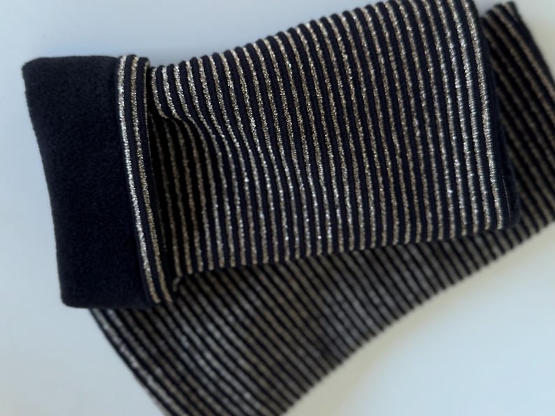 Puede incluir: Un par de calentadores de brazo a rayas negras y plateadas. Los calentadores de brazo est&aacute;n hechos de una tela suave y el&aacute;stica y tienen una textura acanalada.