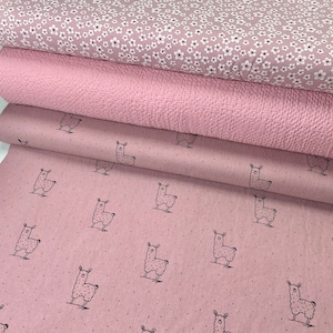 Könnte beinhalten: Vier Rollen rosa Stoff mit verschiedenen Mustern. Die oberste Rolle hat einen kleinen weißen Blumendruck. Die zweite Rolle hat eine strukturierte Oberfläche. Die dritte und vierte Rolle haben einen rosa Hintergrund mit schwarzen Lama-Silhouetten.