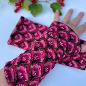 May include: A pair of pink and black patterned fingerless gloves. The gloves have a floral design with a black background.