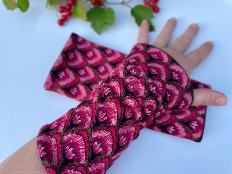 May include: A pair of pink and black patterned fingerless gloves. The gloves have a floral design with a black background.
