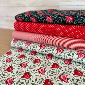 Könnte beinhalten: Ein Stapel Stoffballen mit verschiedenen Mustern. Der oberste Ballen hat einen marineblauen Hintergrund mit roten Erdbeeren und grünen Blättern. Weitere Stoffe sind rote Punkte, rosa Streifen und ein weißer Hintergrund mit roten Erdbeeren und grünen Blättern.