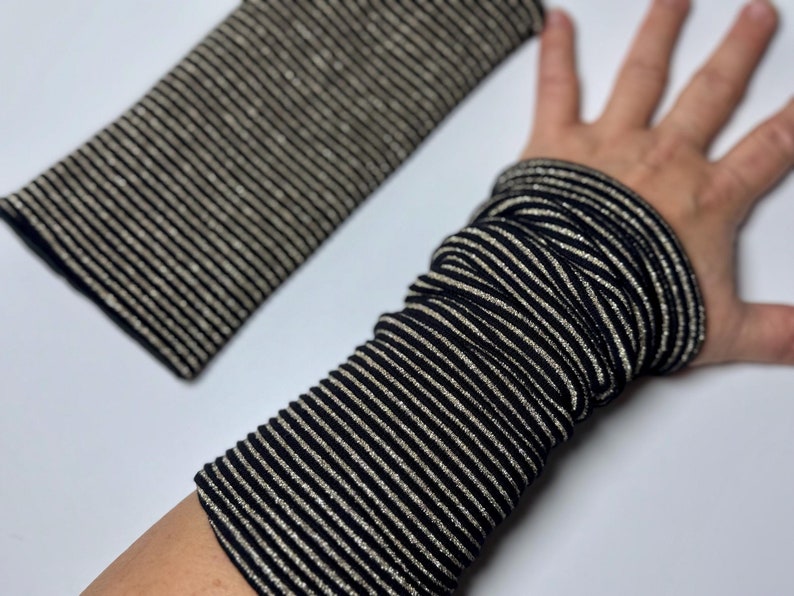 Puede incluir: Calentadores de brazo a rayas negras y doradas. Los calentadores est&aacute;n hechos de un tejido el&aacute;stico y tienen un brillo sutil.