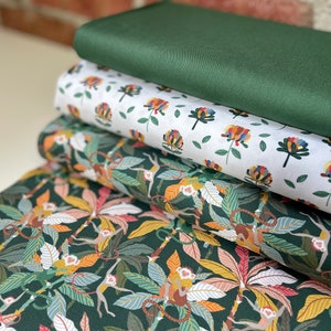 Könnte beinhalten: Ein Stapel von vier Stoffmustern mit verschiedenen Mustern. Das oberste Muster ist einfarbig dunkelgrün, das zweite ist weiß mit einem bunten Blumenmuster, das dritte ist dunkelgrün mit einer Dschungelszene mit Affen und Blättern, und das unterste Muster ist dunkelgrün mit einem abstrakteren Muster aus Blättern und Ranken.