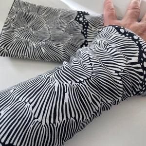 May include: Black and white arm warmers with a wavy, abstract pattern. The fabric is soft and stretchy.