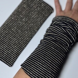 Puede incluir: Un par de calentadores de brazo a rayas negras y plateadas. Los calentadores de brazo est&aacute;n hechos de una tela suave y el&aacute;stica y tienen un brillo sutil.
