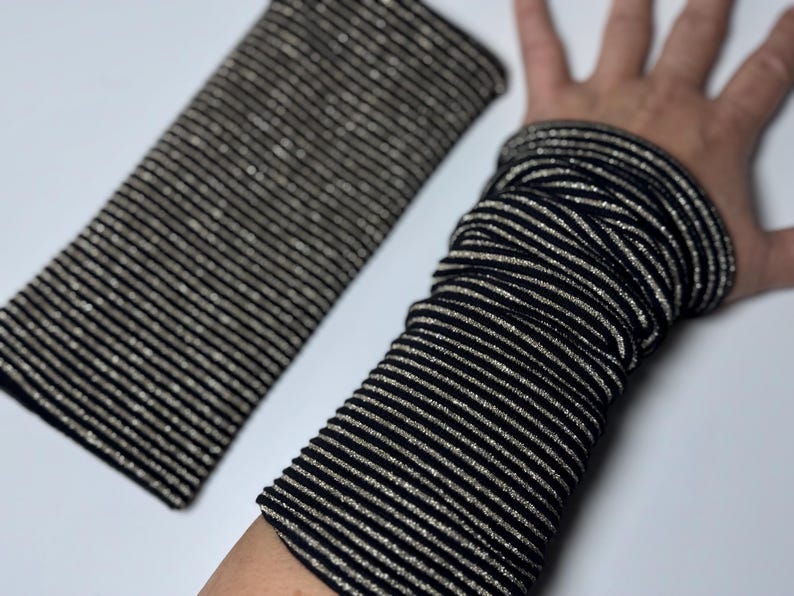 Puede incluir: Un par de calentadores de brazo a rayas negras y plateadas. Los calentadores de brazo est&aacute;n hechos de una tela suave y el&aacute;stica y tienen un brillo sutil.