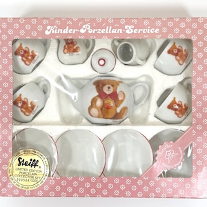 May include: A boxed Steiff limited edition porcelain collector set. The set includes a teapot, cups, saucers, and a creamer, all decorated with a teddy bear design. The box is pink with a floral pattern and the text "Kinder-Porzellan-Service".