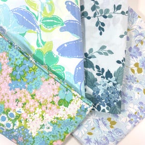 May include: Four folded fabric pieces with floral patterns in shades of blue, green, and pink. The patterns include large stylized flowers, delicate blossoms, and leafy designs. The fabrics appear to be cotton or a similar material.