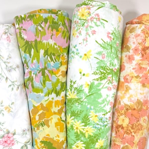 Puede incluir: Cuatro rollos de tela floral vintage. Las telas presentan varios estampados florales en tonos rosa, amarillo, verde y naranja. Las telas están bien enrolladas, mostrando los diferentes diseños y colores.