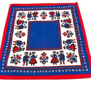 Può includere: Fazzoletto quadrato con bordo rosso e centro blu. La sezione bianca presenta figure di arte popolare in abiti tradizionali, fiori rossi e dettagli blu. Il bordo ha un motivo di piccoli fiori gialli.