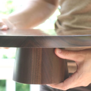 May include: A dark brown wooden cake stand with a round top and a pedestal base. The stand is made of walnut wood and has a smooth, polished finish.