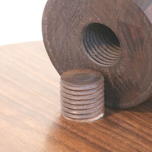 May include: Close-up of a wooden table leg with a threaded insert. The leg is made of dark wood and has a smooth finish. The insert is made of metal and has a threaded design.