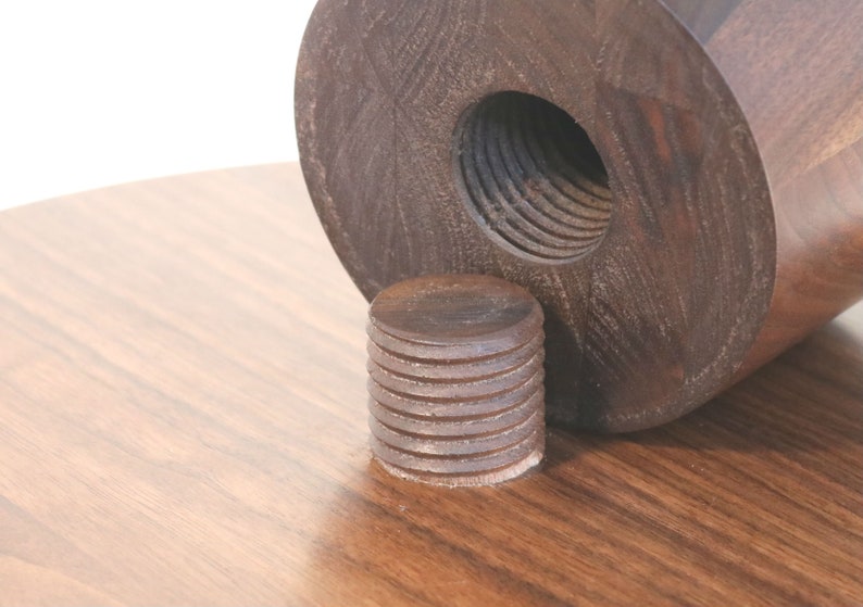 May include: Close-up of a wooden table leg with a threaded insert. The leg is made of dark wood and has a smooth finish. The insert is made of metal and has a threaded design.