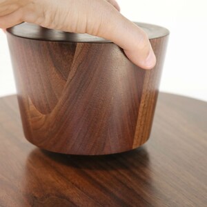 May include: A dark brown wooden bowl with a lid, the lid is being lifted by a hand.