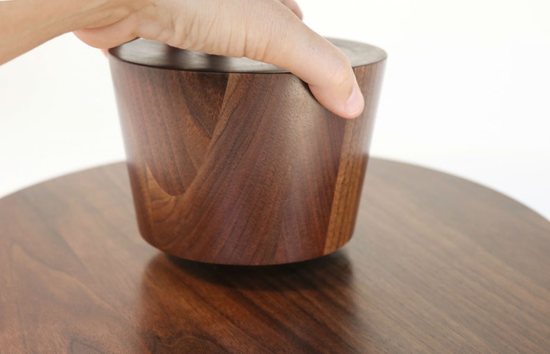 May include: A dark brown wooden bowl with a lid, the lid is being lifted by a hand.