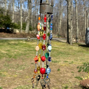 May include: A colorful beaded wind chime with a metal top and multiple keys hanging from the bottom. The beads are red, orange, yellow, green, blue, and purple.
