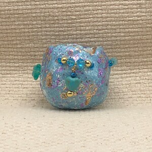 May include: A small, blue, round ceramic planter with gold and turquoise accents. The planter is decorated with gold glitter and has a turquoise heart in the center.