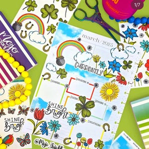 May include: A colorful planner with a March 2025 calendar page, decorated with stickers featuring rainbows, shamrocks, flowers, and a pot of gold. The planner has a section labeled "Currently" with boxes for "Dreaming", "Reflecting on", "Playing", "Listening to", and "Decluttering". The planner also has a sticker that says "Shine Bright".