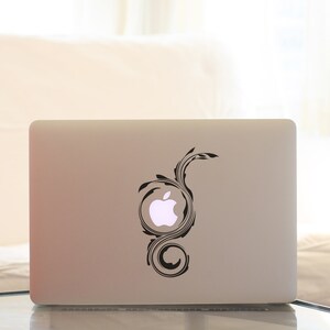 May include: A silver laptop computer with a black and white swirl design sticker on the lid. The sticker features a stylised apple logo in the centre.