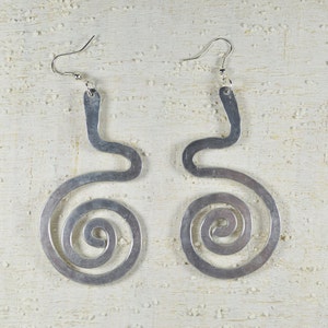 Puede incluir: Un par de pendientes de plata con un dise&ntilde;o &uacute;nico. Cada pendiente tiene una forma curva y abierta con una espiral en la parte inferior.