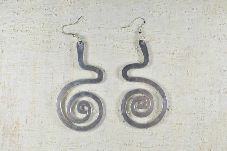 Puede incluir: Un par de pendientes de plata con un dise&ntilde;o &uacute;nico. Cada pendiente tiene una forma curva y abierta con una espiral en la parte inferior.