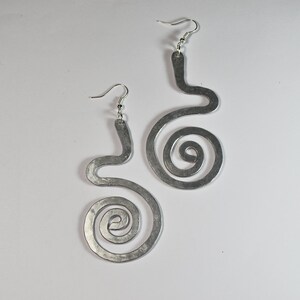 Puede incluir: Un par de pendientes de plata con un dise&ntilde;o &uacute;nico y abstracto. Cada pendiente tiene una forma curva con una espiral en la parte inferior.