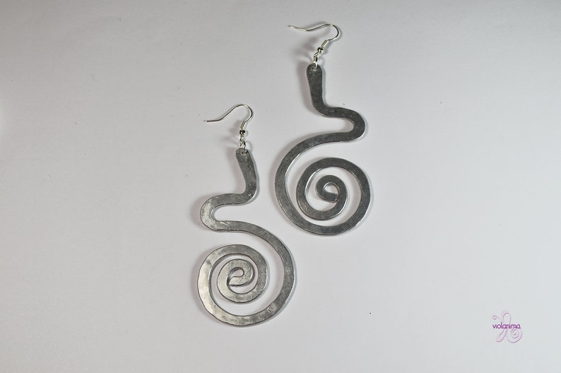 Puede incluir: Un par de pendientes de plata con un dise&ntilde;o &uacute;nico y abstracto. Cada pendiente tiene una forma curva con una espiral en la parte inferior.