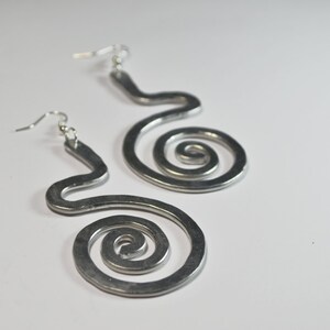 Puede incluir: Un par de pendientes de plata con un dise&ntilde;o en espiral. Los pendientes est&aacute;n hechos de metal y tienen un aspecto simple y moderno.