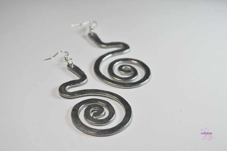 Puede incluir: Un par de pendientes de plata con un dise&ntilde;o en espiral. Los pendientes est&aacute;n hechos de metal y tienen un aspecto simple y moderno.