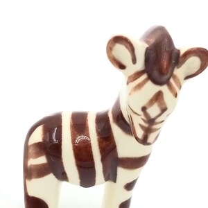 May include: A small ceramic zebra figurine with brown and white stripes. The zebra is standing on all four legs and has a brown head with white stripes.
