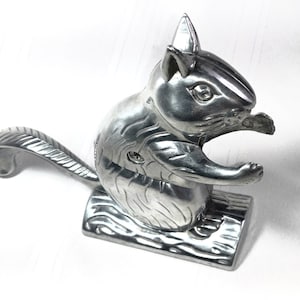 May include: A silver squirrel nutcracker with a detailed design. The squirrel is holding a nut in its mouth and has a lever on its back to crack the nut.