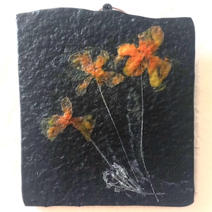 May include: Three pressed orange and yellow flowers on a black textured background.
