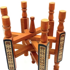 May include: A wooden decorative stand with a geometric design. The stand is made of light brown wood with dark brown and gold inlay details. The stand has six legs and a central support, and is approximately 8 inches tall.