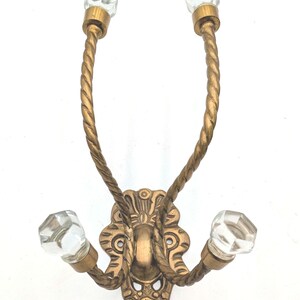 May include: Antique-style wall hook with a decorative brass finish. The hook features three clear, faceted crystal knobs and twisted rope-like arms. The ornate backplate adds to the vintage aesthetic, perfect for adding a touch of elegance to any space.