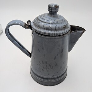 May include: A vintage gray enamelware coffee pot with a lid and handle. The pot has a spout for pouring and a speckled pattern on the lid and body. The handle and lid knob are a lighter shade of gray.