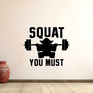 Può includere: Adesivo da parete in bianco e nero con la silhouette di un personaggio immaginario che solleva un bilanciere con il testo "SQUAT YOU MUST".