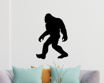 Könnte beinhalten: Schwarze Silhouette von Bigfoot, der auf einer weißen Wand nach rechts geht. Die Silhouette ist ein Wandaufkleber. Im Vordergrund befindet sich eine Couch mit Kissen.