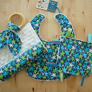 May include: A baby gift set with a blue and green star print. The set includes a bib, a burp cloth, a teether, and a soft toy. The items are all made of soft, comfortable fabric.