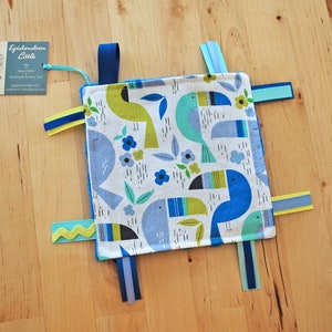 Könnte beinhalten: Ein blaues und grünes Stoffspielzeug für Babys mit Tukanen und Blumen. Das Spielzeug hat mehrere Bänder daran befestigt.