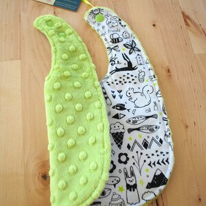 May include: A reversible baby bib with a lime green soft, textured side and a white side with black and white illustrations of animals, stars, and other designs. The text "best friends" is visible on the white side.