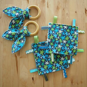 May include: A baby toy with a blue and green starfish pattern. The toy has two wooden rings and several fabric ribbons attached.