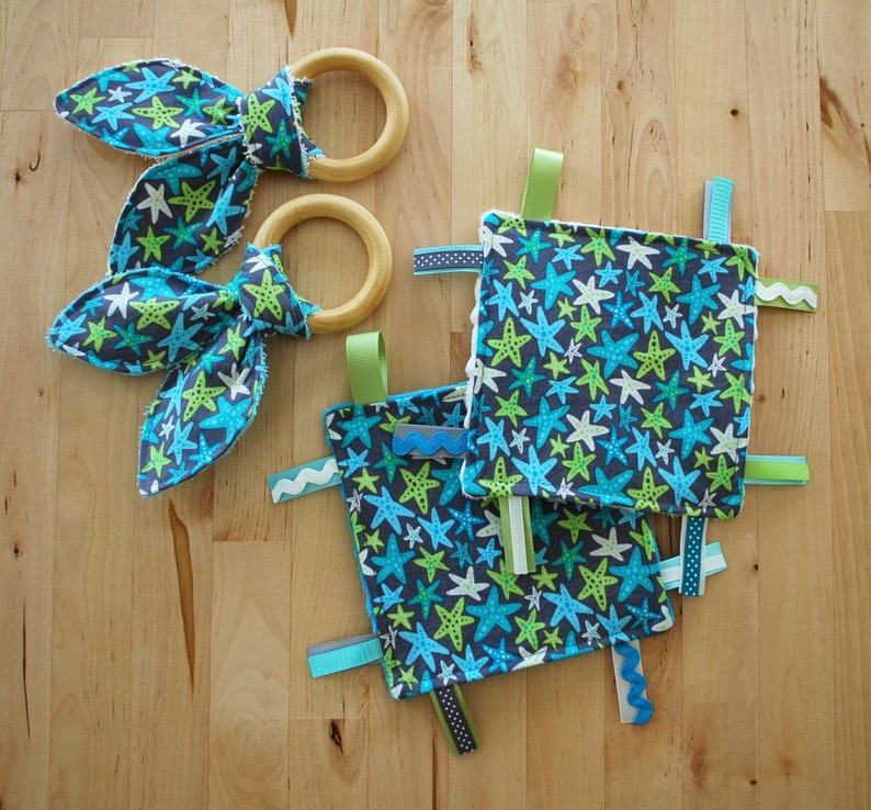 May include: A baby toy with a blue and green starfish pattern. The toy has two wooden rings and several fabric ribbons attached.