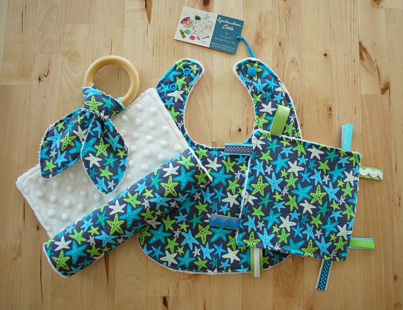 May include: A baby gift set with a blue and green star print. The set includes a bib, a burp cloth, a teether, and a soft toy. The items are all made of soft, comfortable fabric.