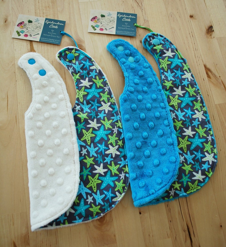 May include: Three baby bibs with a blue and green starfish pattern. One bib is white, one is blue, and one is blue with a white dot pattern. The bibs have a snap closure.