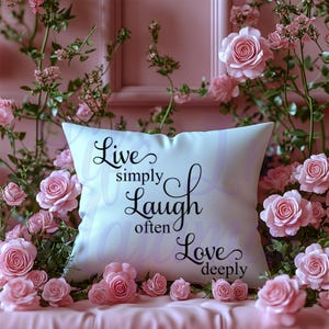 May include: White cushion with black text that reads "Live simply, Laugh often, Love deeply" surrounded by pink roses.