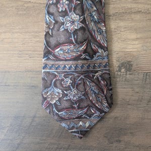 May include: A patterned necktie with a dark brown background and floral and leaf designs in shades of blue, red, and brown. The tie has a pointed end and a repeating geometric border.