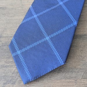 May include: A navy blue tie with a light blue plaid pattern. The tie is made of a smooth fabric and is angled towards the bottom right corner, resting on a wooden surface.