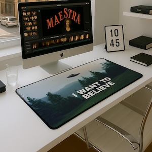 Puede incluir: Un escritorio con una computadora, un vaso de agua y una alfombrilla de ratón con una escena de bosque y el texto "I WANT TO BELIEVE".